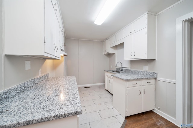 kitchen with visible vents, wainscoting, a decorative wall, white cabinetry, and a sink