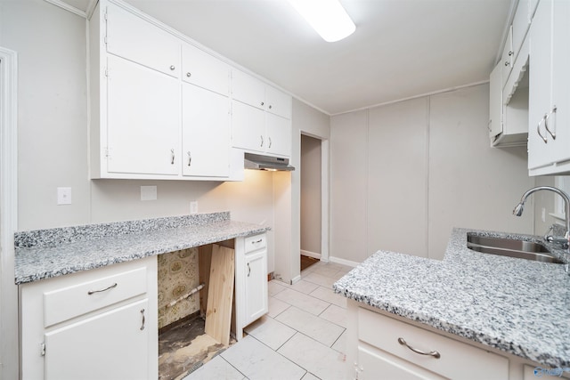 kitchen with light stone countertops, light tile patterned floors, built in desk, white cabinetry, and a sink