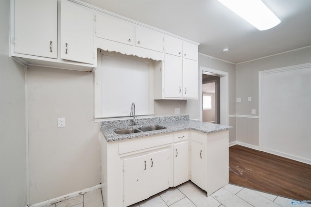 kitchen with light stone countertops, light wood-type flooring, ornamental molding, white cabinets, and a sink