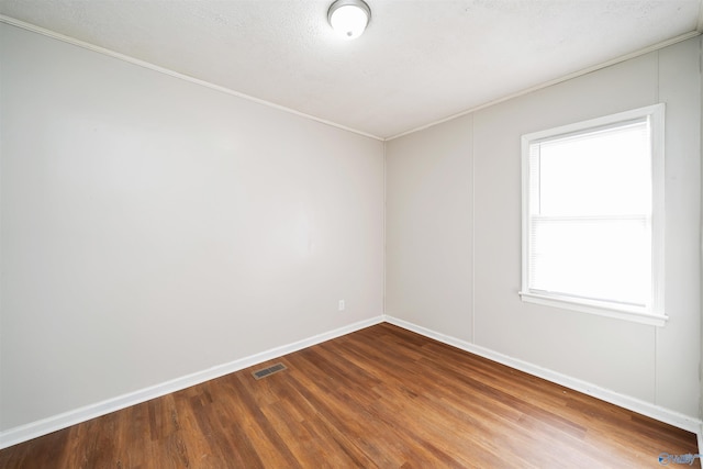 spare room featuring visible vents, baseboards, a textured ceiling, and wood finished floors