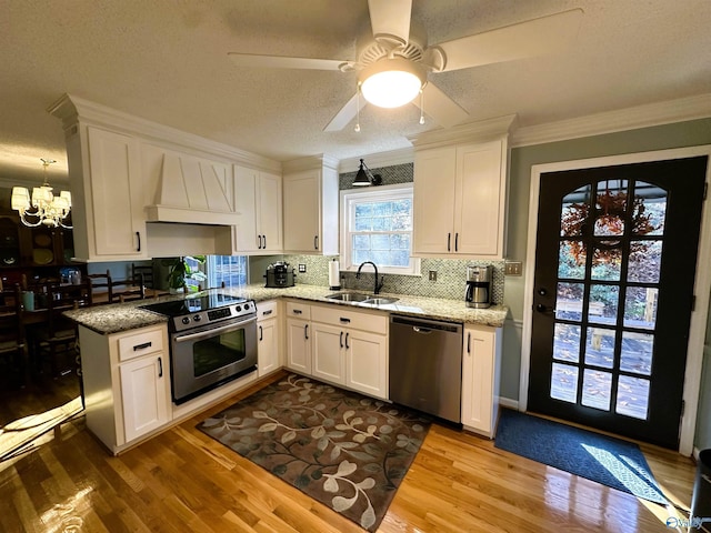 kitchen featuring appliances with stainless steel finishes, light stone countertops, custom exhaust hood, white cabinetry, and a sink