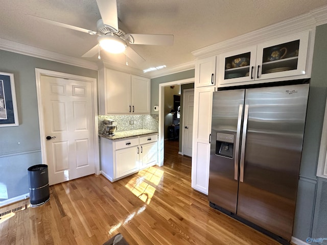 kitchen with light stone counters, white cabinetry, light wood-style floors, stainless steel fridge with ice dispenser, and crown molding