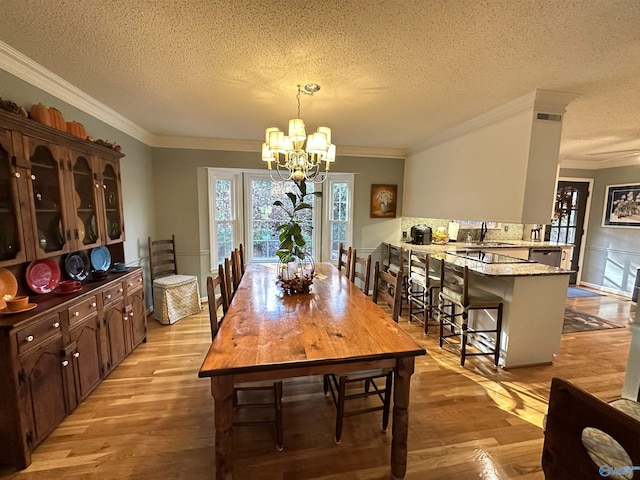 dining area featuring a textured ceiling, visible vents, ornamental molding, light wood finished floors, and an inviting chandelier