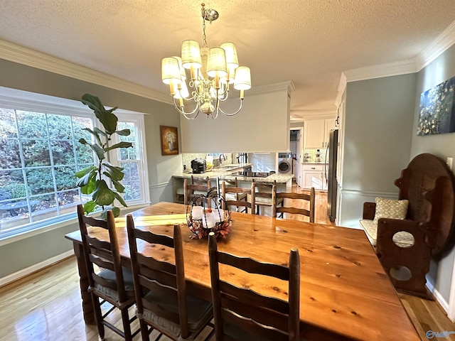 dining space featuring a notable chandelier, washer / clothes dryer, ornamental molding, a textured ceiling, and light wood-type flooring