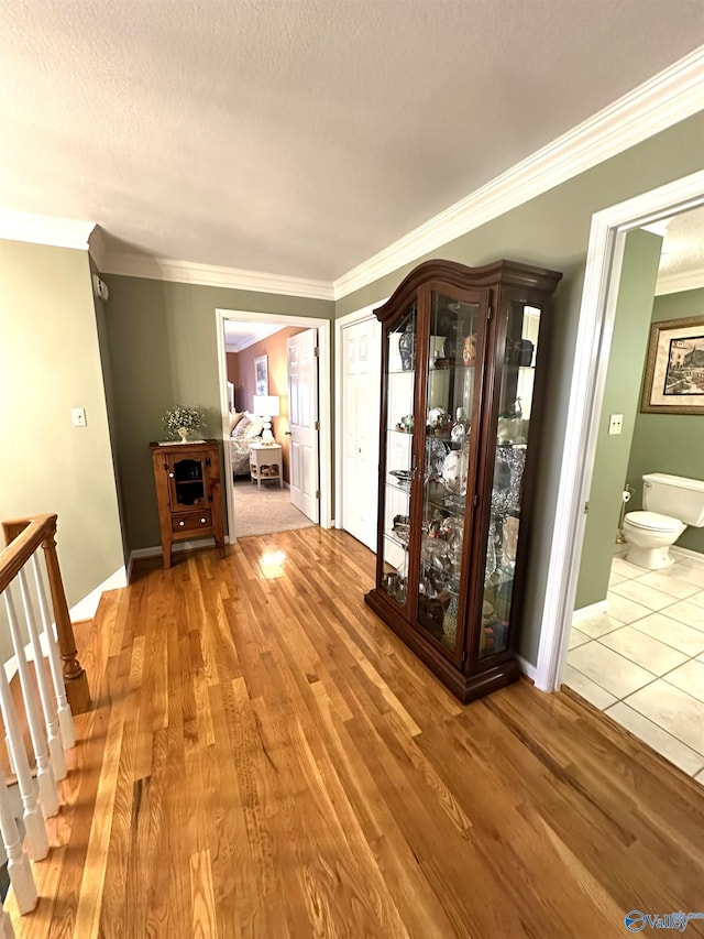 corridor with ornamental molding, wood finished floors, and an upstairs landing