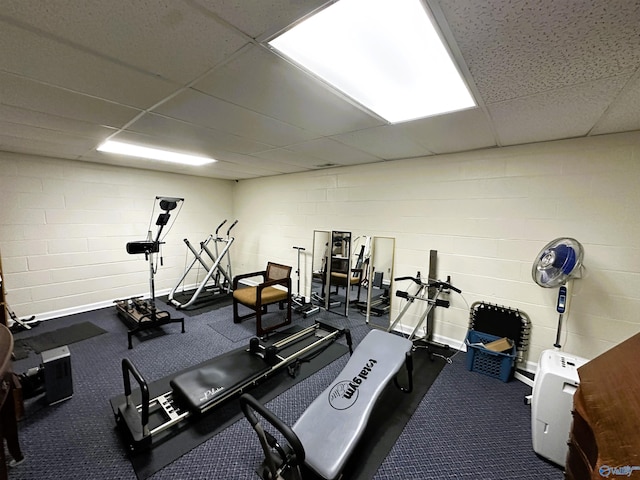 exercise room featuring concrete block wall and a paneled ceiling