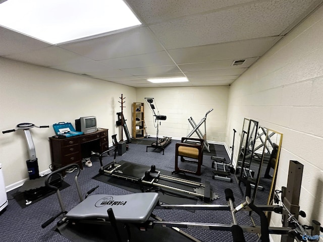 exercise room featuring baseboards, a paneled ceiling, visible vents, and concrete block wall