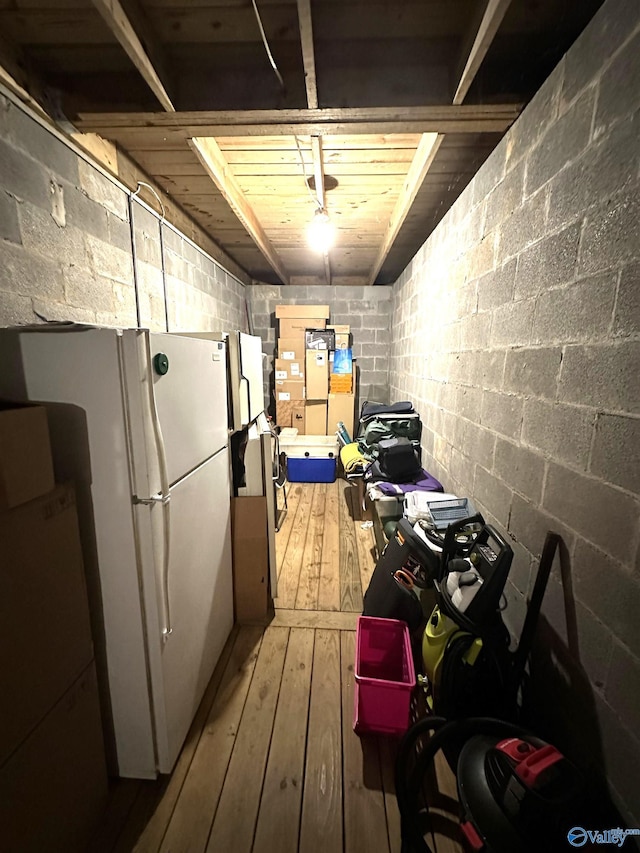 interior space featuring concrete block wall, wood finished floors, and freestanding refrigerator