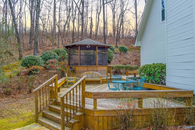 deck at dusk featuring a sunroom, outdoor dining space, and a gazebo