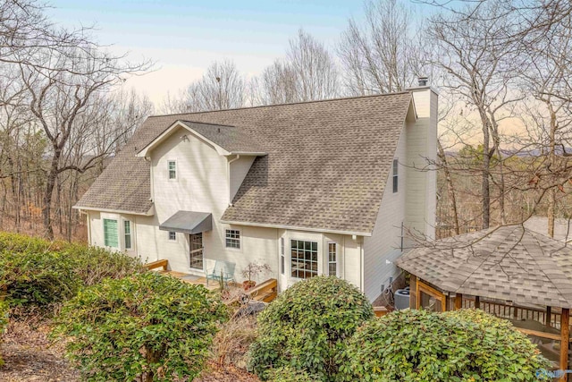 back of property at dusk with a shingled roof, a chimney, and central air condition unit