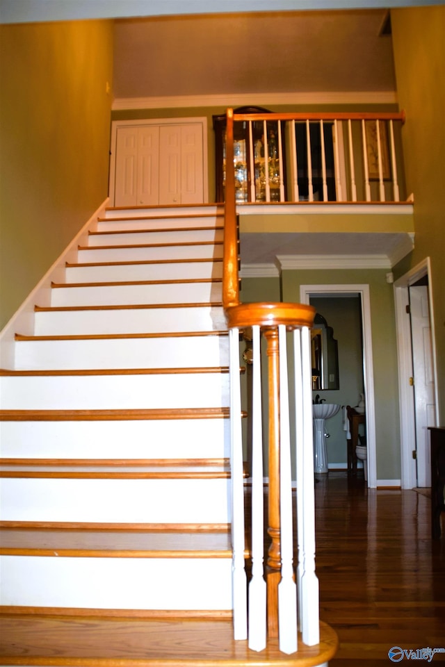 stairway with crown molding and wood finished floors