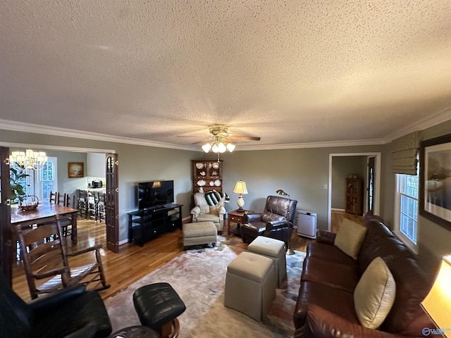 living room with crown molding, a textured ceiling, wood finished floors, plenty of natural light, and ceiling fan with notable chandelier