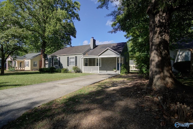 ranch-style house with driveway, a chimney, a front lawn, stone siding, and covered porch