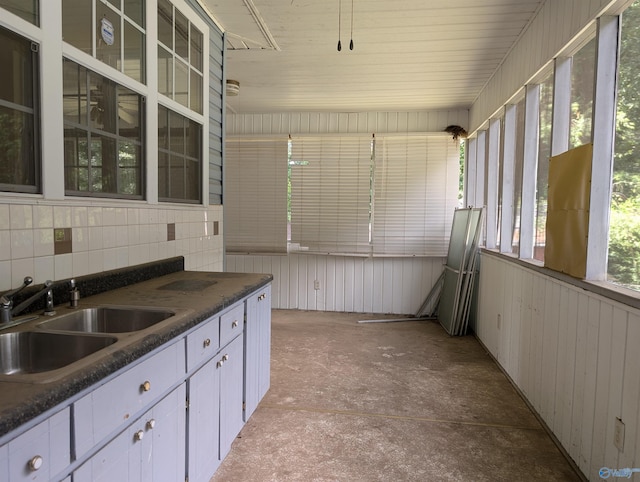 kitchen with dark stone counters, sink, wooden walls, and white cabinets