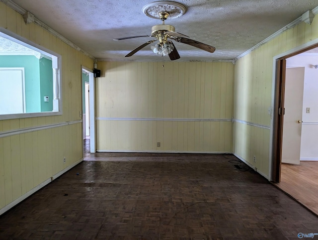 unfurnished room featuring wooden walls, crown molding, ceiling fan, dark parquet flooring, and a textured ceiling