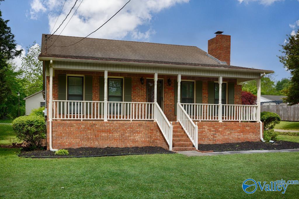 view of front facade featuring a front lawn, a chimney, covered porch, and brick siding