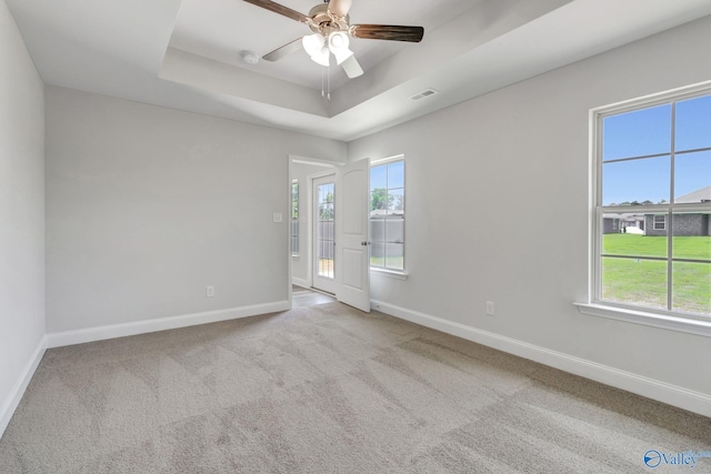 carpeted empty room featuring visible vents, ceiling fan, baseboards, and a tray ceiling