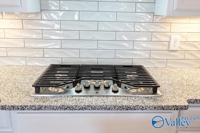 interior details featuring white cabinets, decorative backsplash, light stone counters, and stainless steel gas cooktop