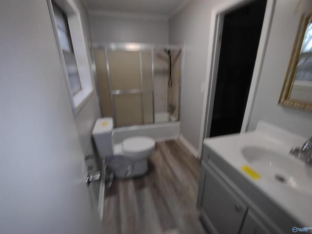 full bath with toilet, wood finished floors, vanity, baseboards, and combined bath / shower with glass door