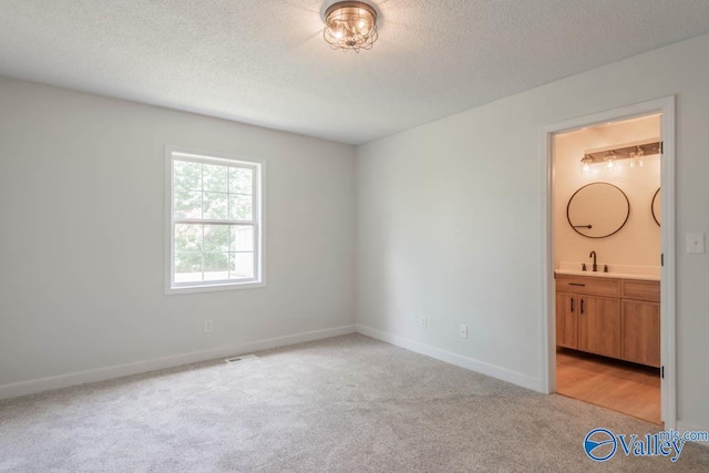 unfurnished bedroom with a textured ceiling, light colored carpet, visible vents, ensuite bathroom, and baseboards