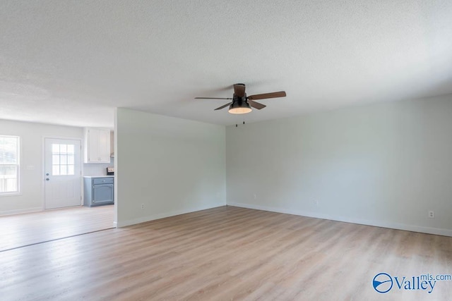 unfurnished living room featuring a textured ceiling, ceiling fan, light wood-style flooring, and baseboards