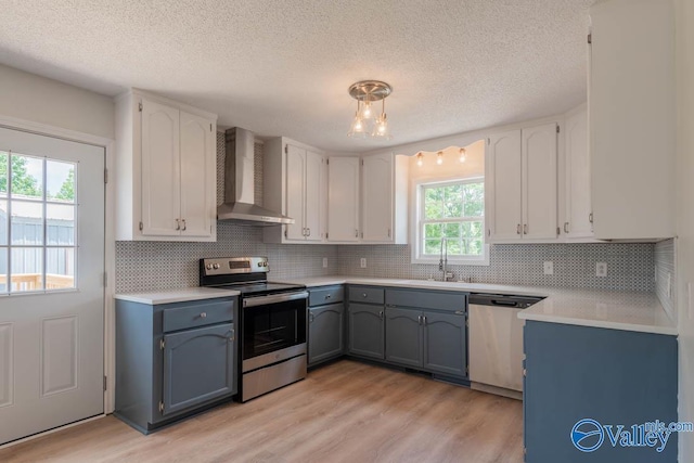 kitchen featuring decorative backsplash, wall chimney exhaust hood, light wood-style flooring, white cabinetry, and appliances with stainless steel finishes