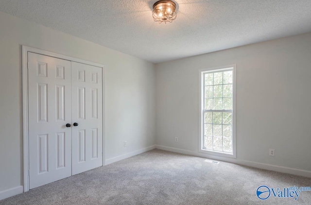 unfurnished bedroom with a textured ceiling, a closet, carpet floors, and baseboards