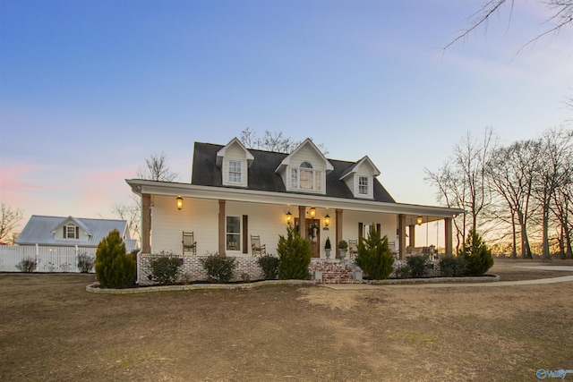 cape cod-style house featuring a lawn and a porch