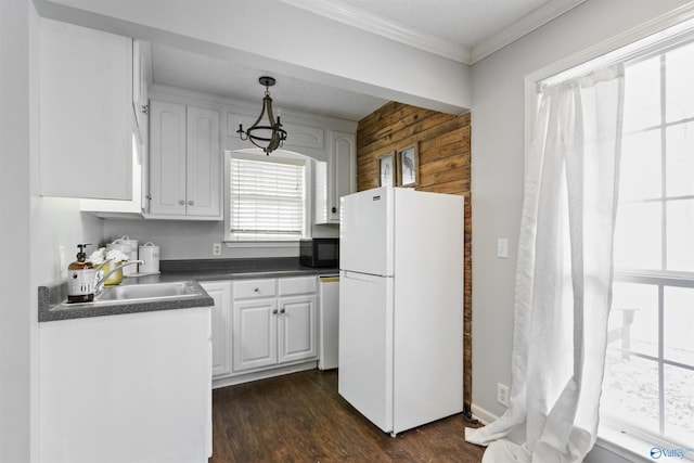 kitchen featuring white refrigerator, sink, hanging light fixtures, and white cabinets