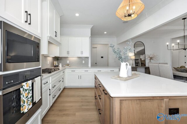 kitchen featuring decorative light fixtures, stainless steel appliances, white cabinets, light hardwood / wood-style flooring, and backsplash