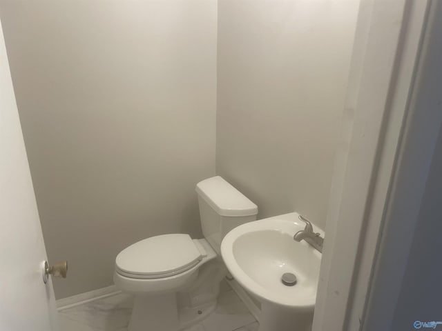 half bath with marble finish floor, baseboards, a sink, and toilet