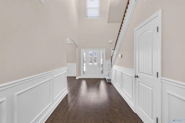 foyer entrance with stairway, arched walkways, dark wood-style flooring, wainscoting, and a decorative wall