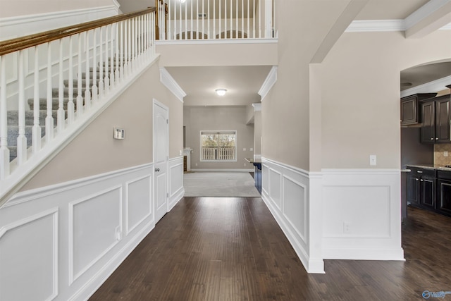 hallway featuring crown molding, a decorative wall, arched walkways, and dark wood-style flooring