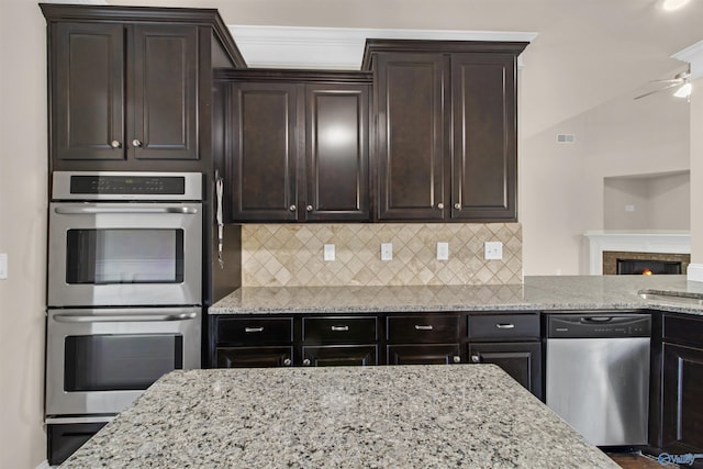 kitchen featuring tasteful backsplash, dark brown cabinets, light stone counters, stainless steel appliances, and a ceiling fan