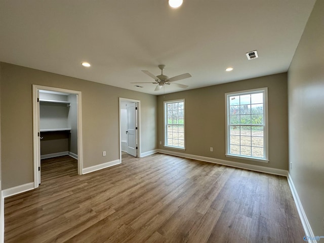 unfurnished bedroom featuring a walk in closet, a closet, light hardwood / wood-style flooring, and ceiling fan