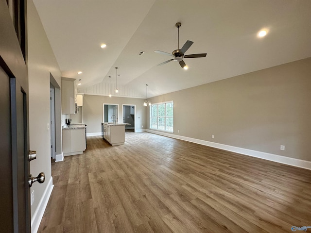 unfurnished living room with ceiling fan with notable chandelier, light wood-type flooring, sink, and high vaulted ceiling