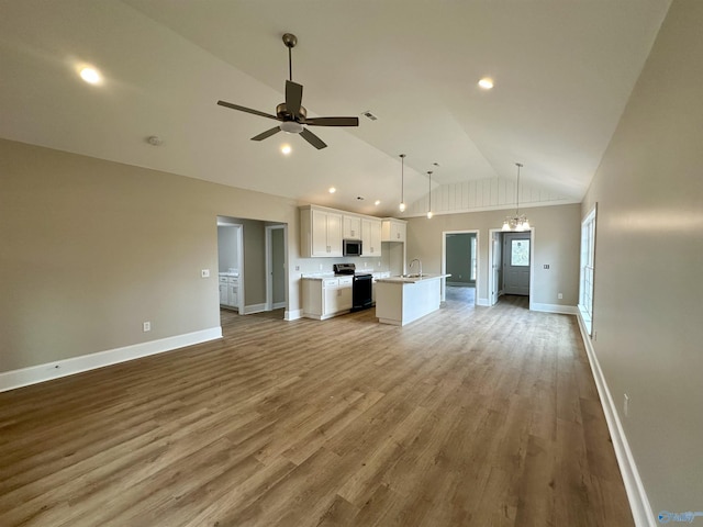 unfurnished living room with hardwood / wood-style floors, ceiling fan with notable chandelier, high vaulted ceiling, and sink