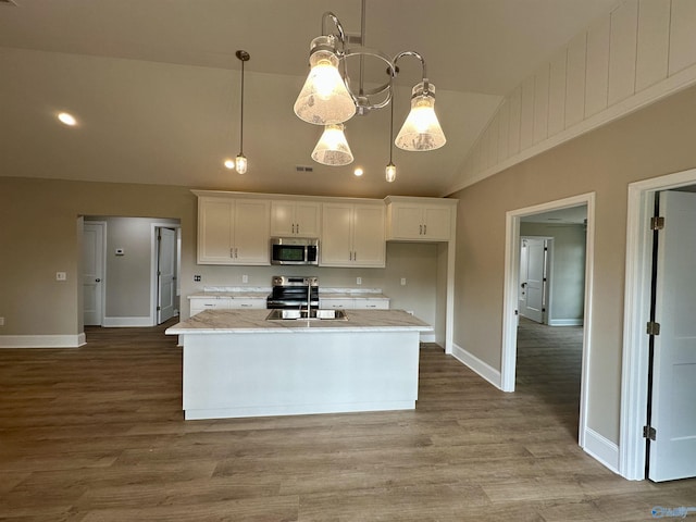 kitchen featuring white cabinetry, stainless steel appliances, light stone counters, vaulted ceiling, and decorative light fixtures