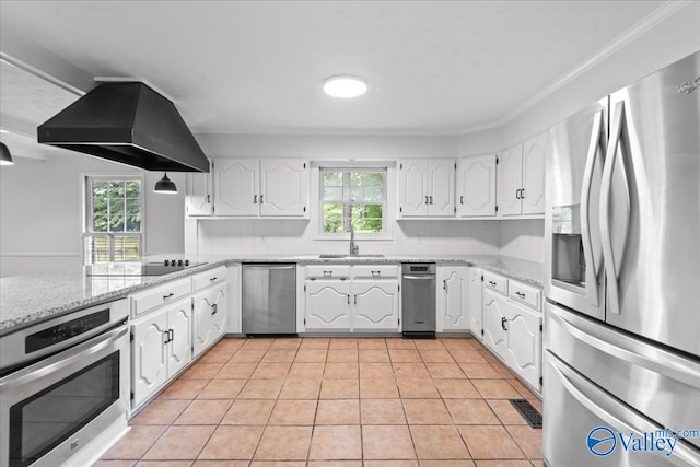 kitchen with appliances with stainless steel finishes, white cabinets, light tile patterned floors, and wall chimney range hood