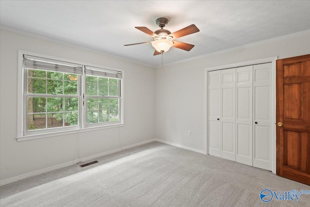 unfurnished bedroom featuring a closet, light colored carpet, crown molding, and ceiling fan