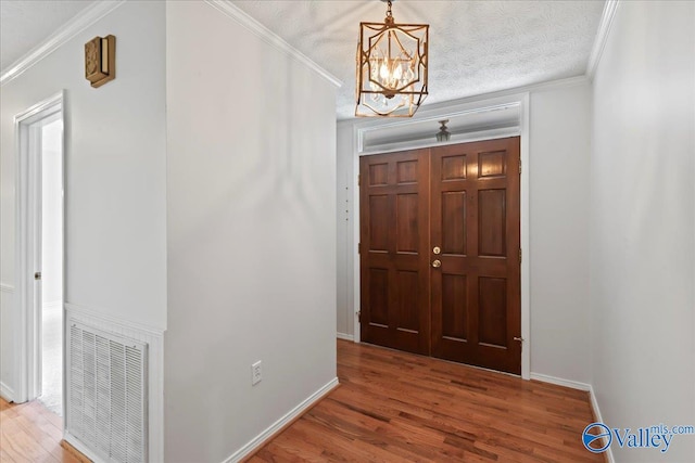 foyer entrance with hardwood / wood-style flooring, ornamental molding, a chandelier, and a textured ceiling