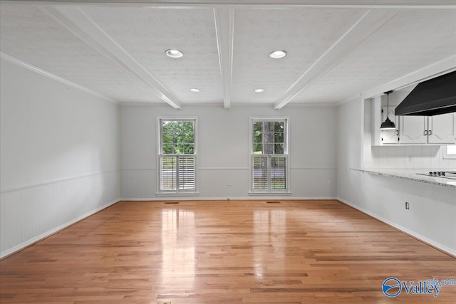 spare room featuring beam ceiling, light hardwood / wood-style floors, and a textured ceiling