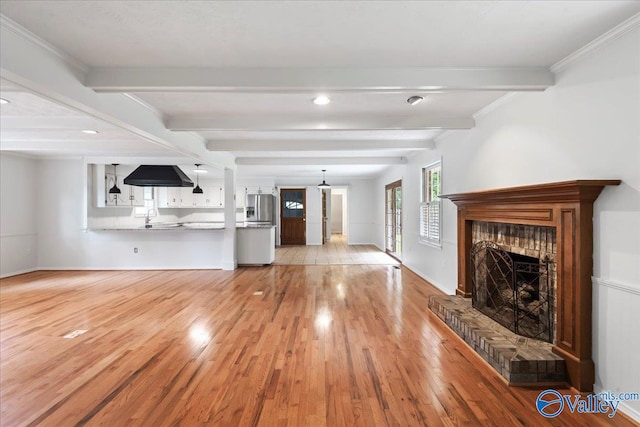 unfurnished living room with light hardwood / wood-style floors, a fireplace, beam ceiling, and crown molding