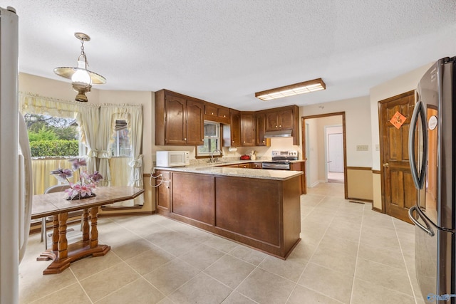 kitchen with appliances with stainless steel finishes, hanging light fixtures, kitchen peninsula, light tile patterned floors, and sink