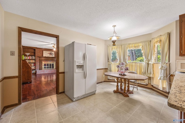 dining area featuring a brick fireplace, a textured ceiling, light hardwood / wood-style flooring, and ceiling fan