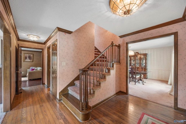 staircase with a textured ceiling, crown molding, and hardwood / wood-style floors