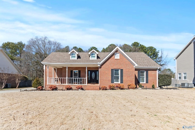 view of front facade featuring covered porch, brick siding, roof with shingles, and a front yard