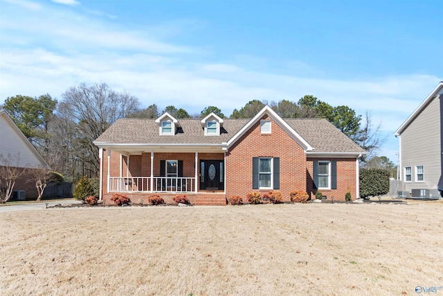 view of front facade featuring covered porch, brick siding, roof with shingles, and a front yard