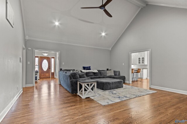 living room featuring high vaulted ceiling, crown molding, baseboards, and wood finished floors