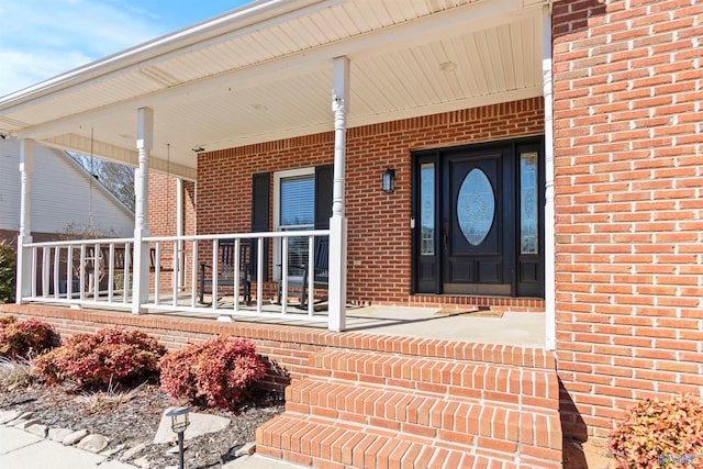 view of exterior entry featuring covered porch and brick siding